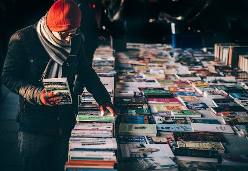 Free Person Holding Book While Browsing on Book Lot Stock Photo