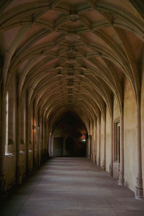 Free A serene view of a Gothic-style cathedral corridor with arched ceilings and historic architecture. Stock Photo