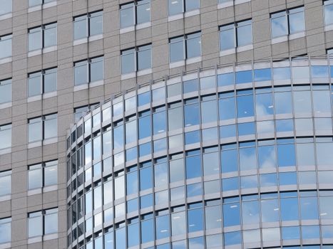 Curved glass facade of a modern office building reflecting the blue sky and clouds.