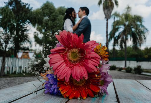 An intimate outdoor wedding scene with a colorful bouquet and a kissing couple in the background.