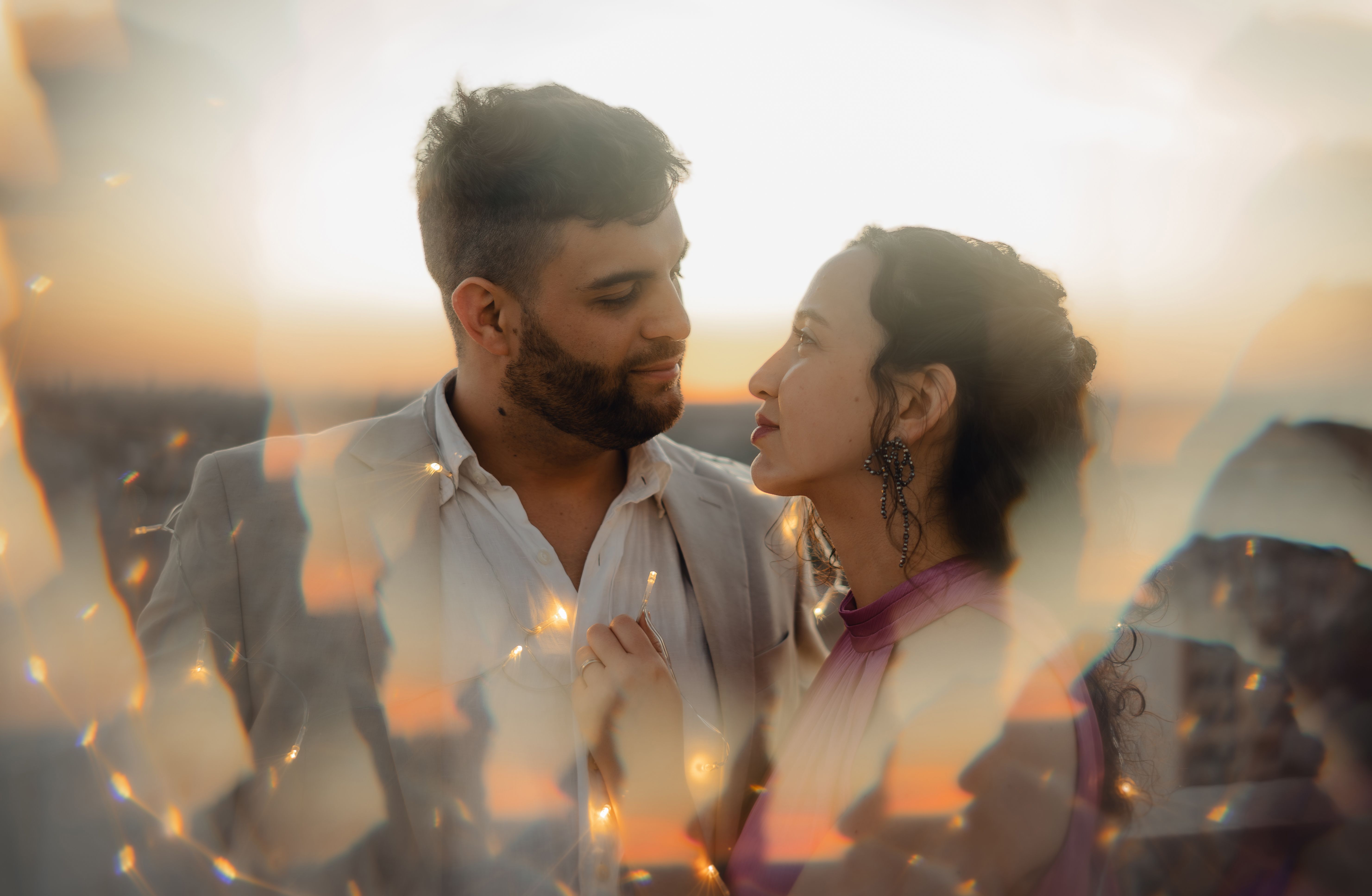 A loving couple gazing at each other, surrounded by warm, dreamy light flares at sunset.