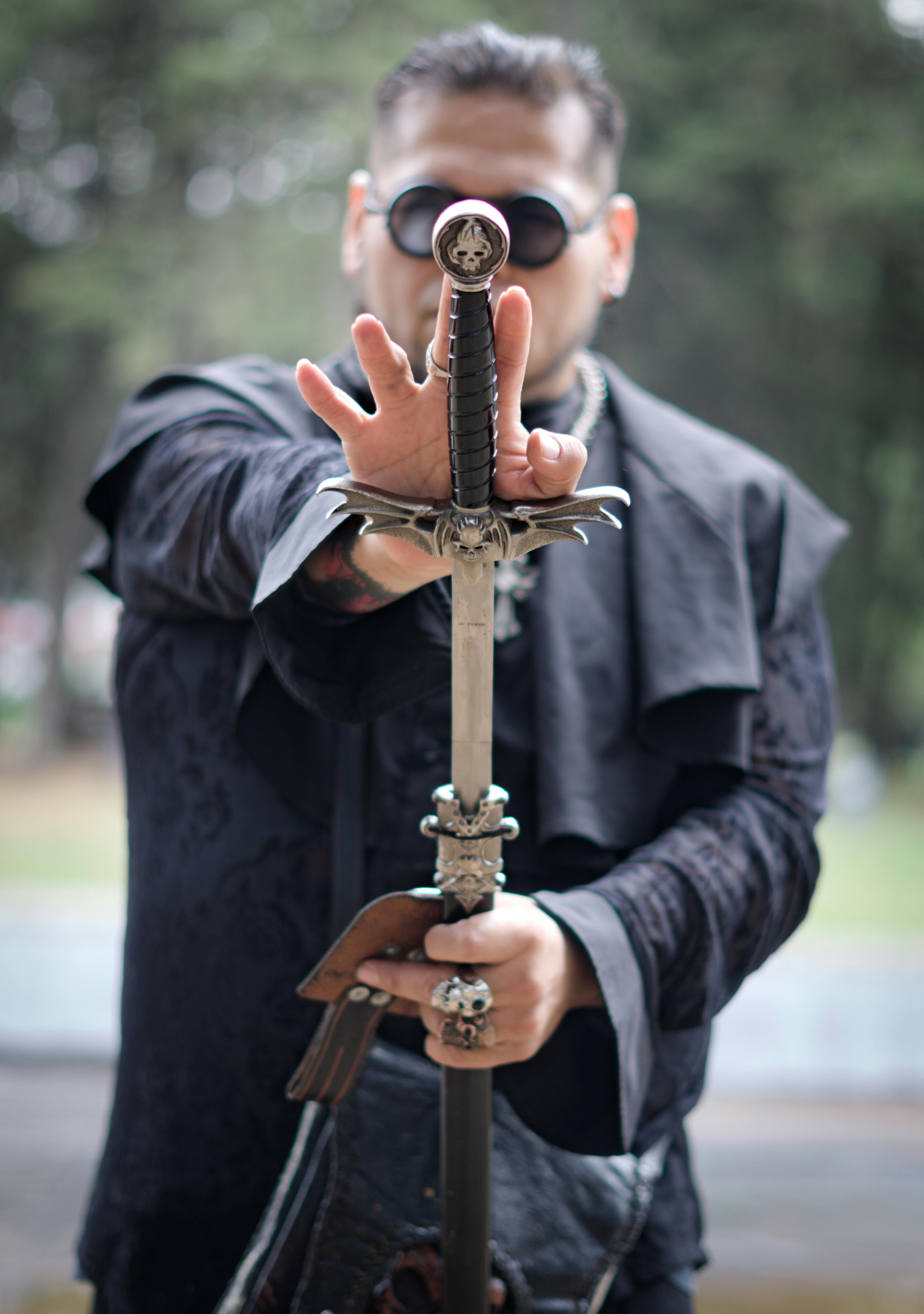 A mysterious man dressed in black holds a sword with a focused expression, creating a dramatic atmosphere.