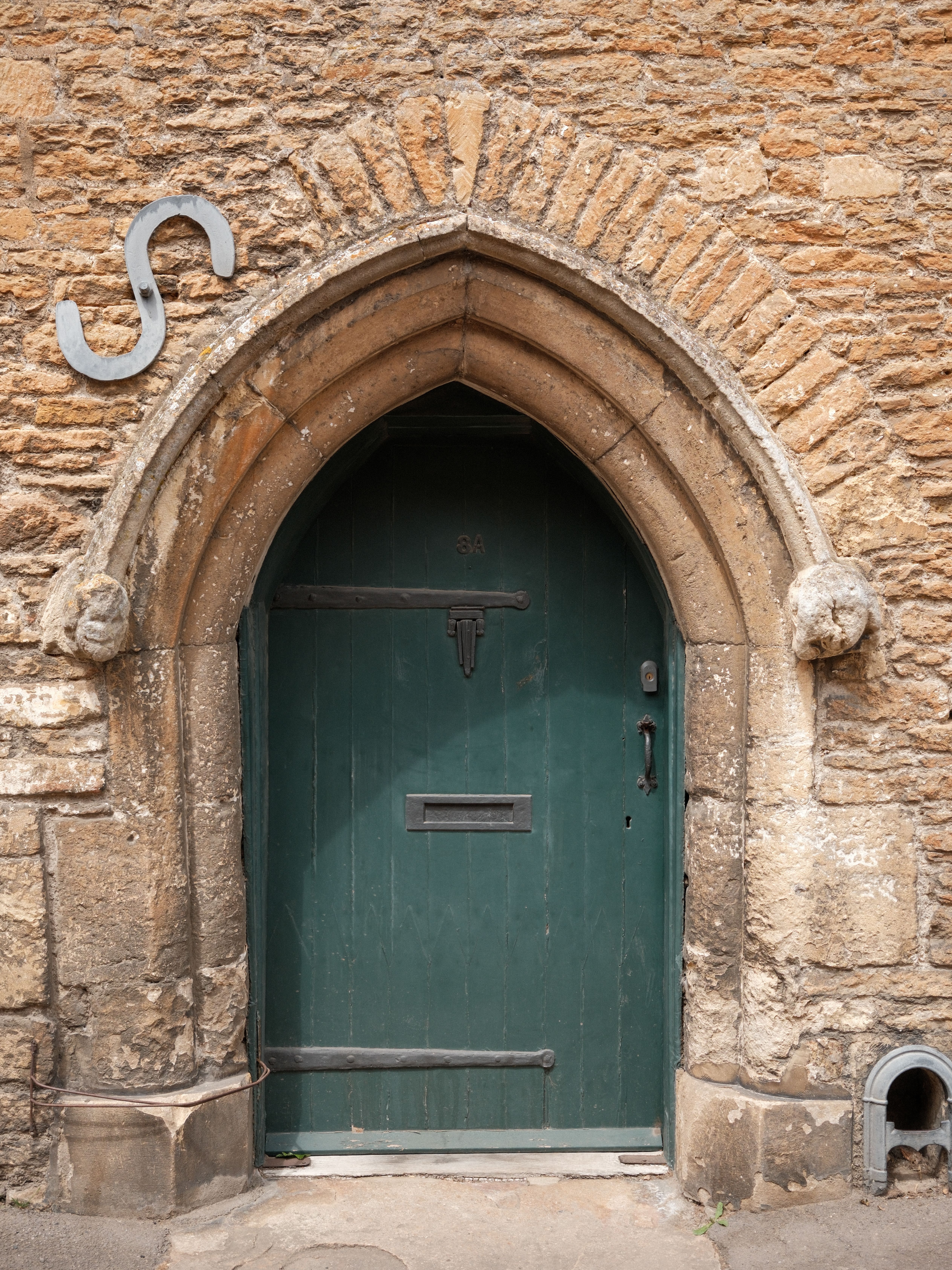 Historic green arched door on stone wall in Lacock, England, showcasing medieval architecture.