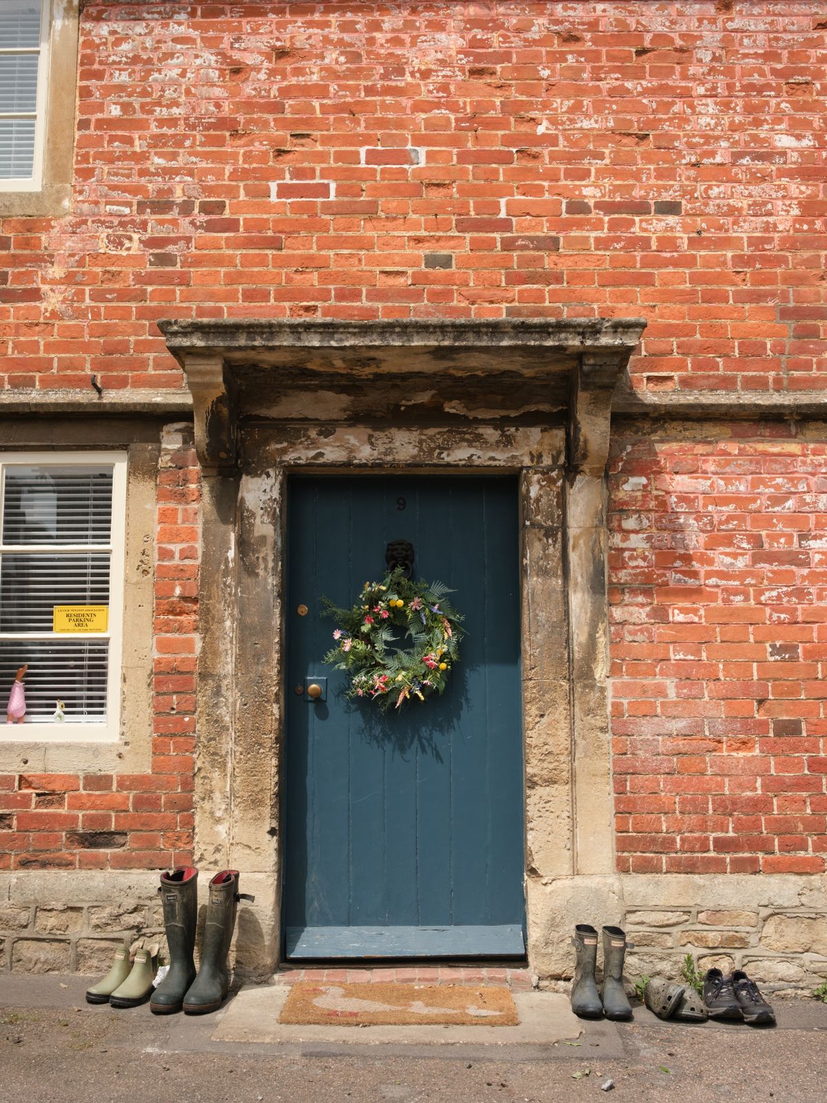 Front view of a traditional English cottage entrance with a blue door and floral wreath. Stock Photo.