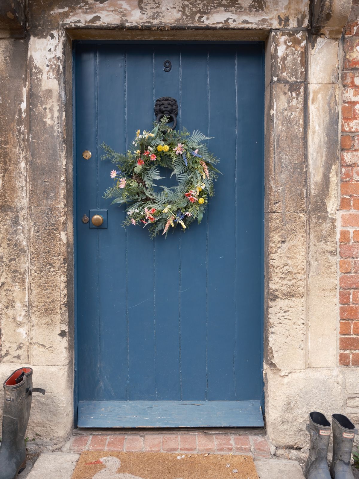 A rustic blue door adorned with a floral wreath in Lacock, England. Stock Photo.