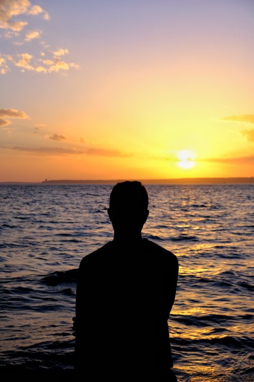 Free Silhouette of a person admiring the vibrant sunset over the ocean, capturing a serene moment. Stock Photo