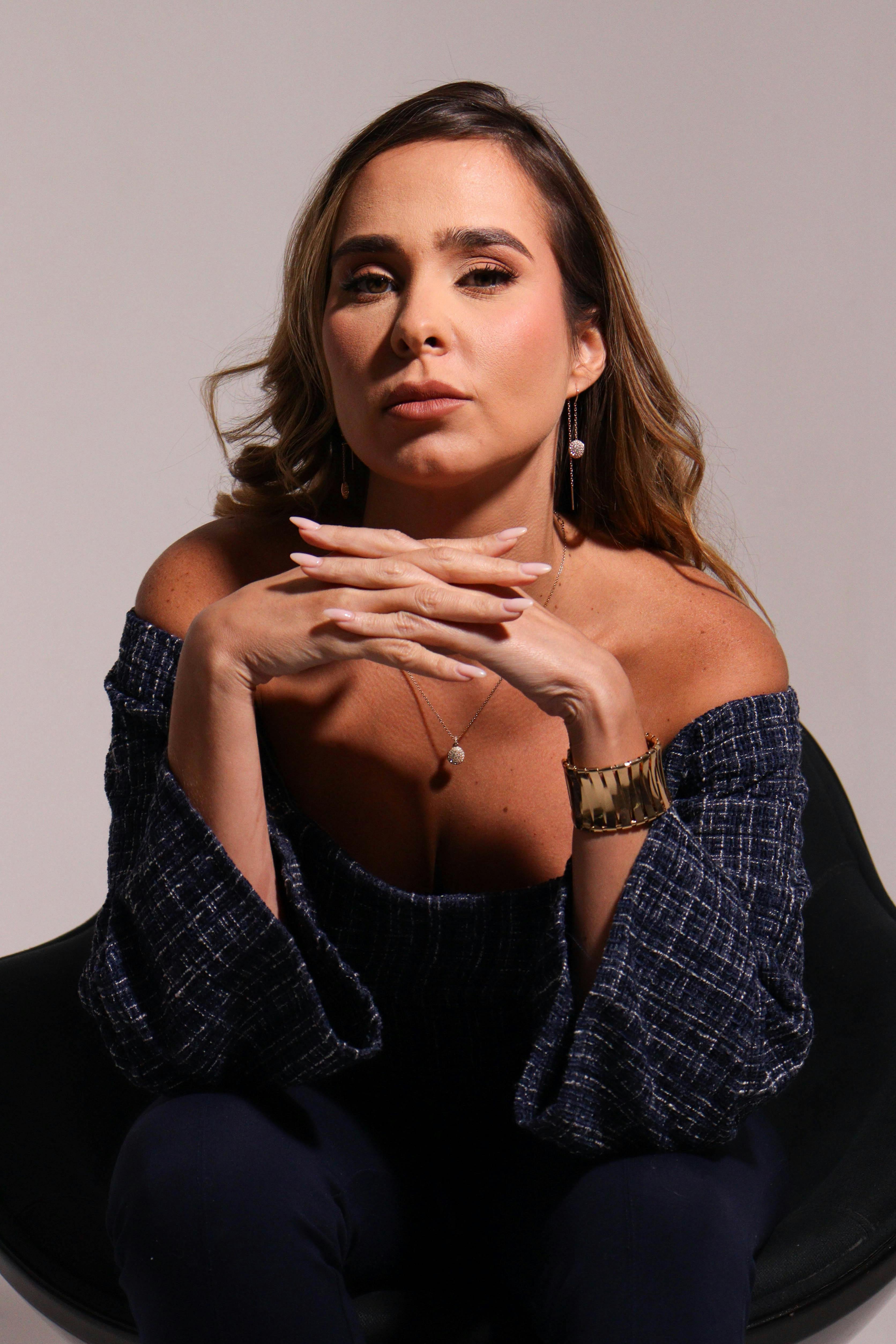 Chic portrait of a woman in an off-shoulder top, seated confidently in a studio chair.