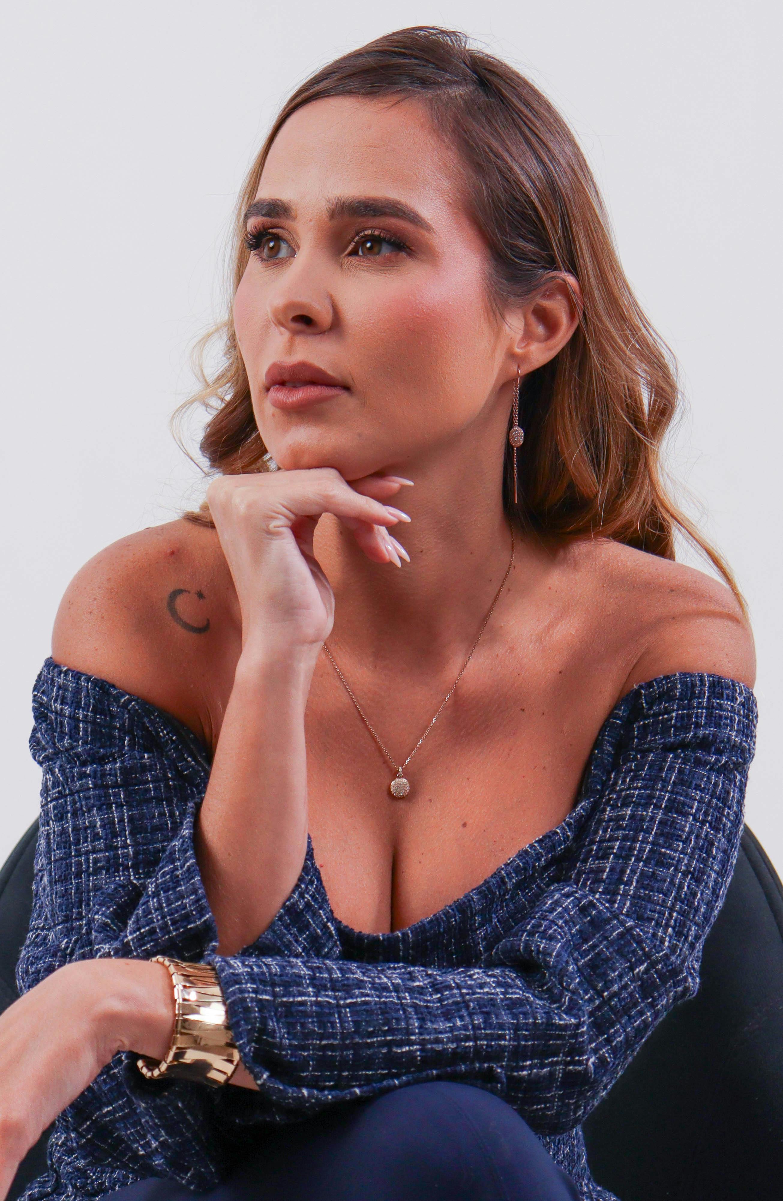 A thoughtful woman in a chic off-shoulder blue top contemplating indoors.