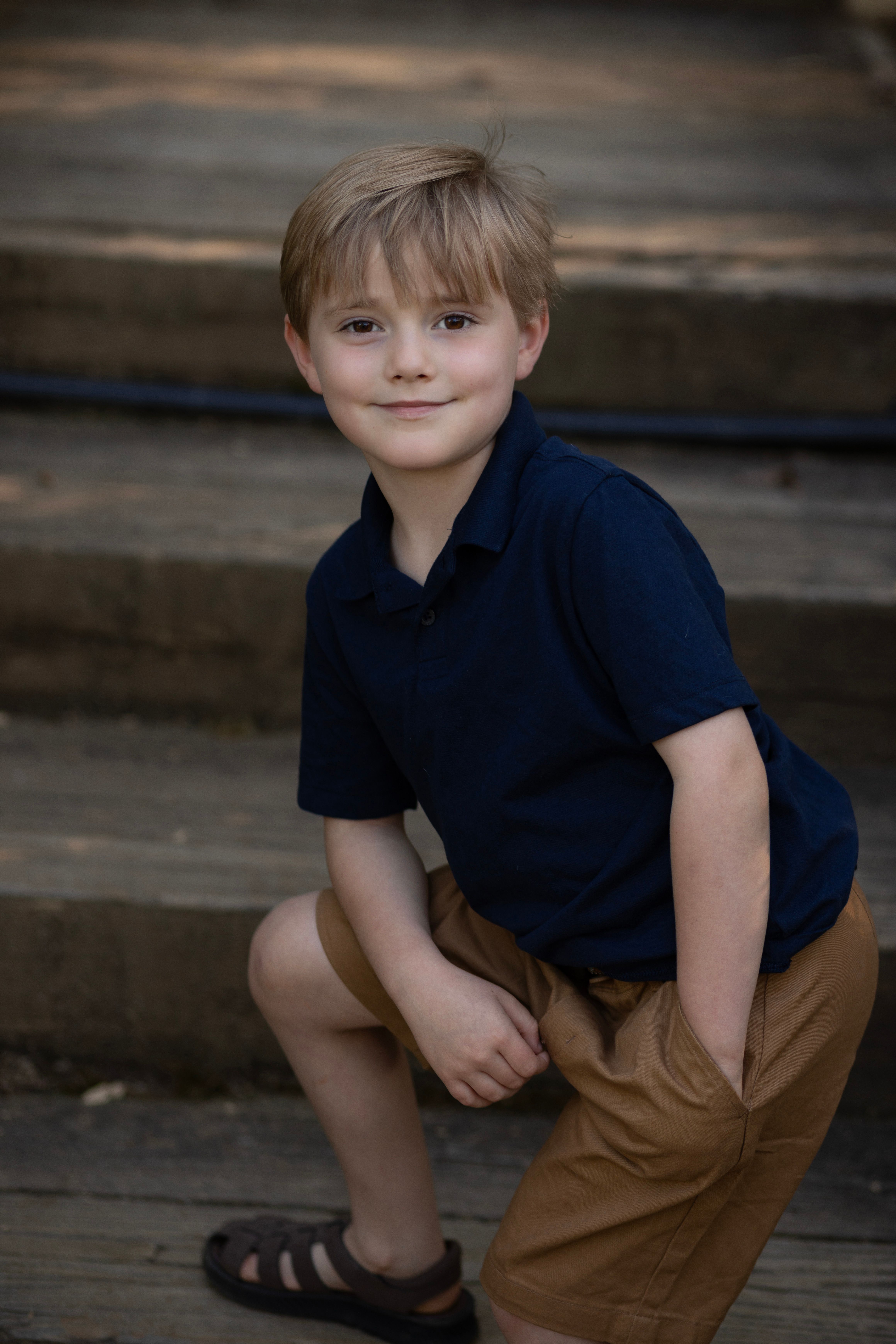 Charming portrait of a young boy in casual clothes sitting on outdoor steps.