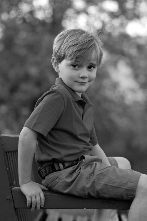 Free Charming black and white portrait of a young boy sitting casually outdoors on a bench. Stock Photo