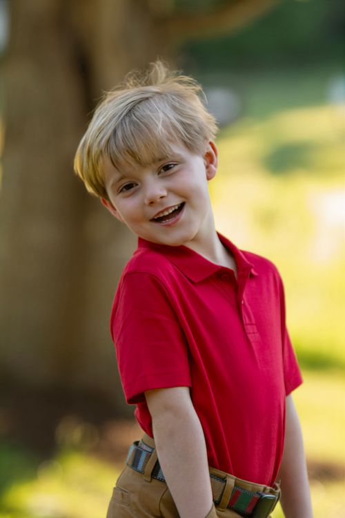 Free A cheerful young boy smiling outdoors in a red polo shirt against a blurred natural background. Stock Photo