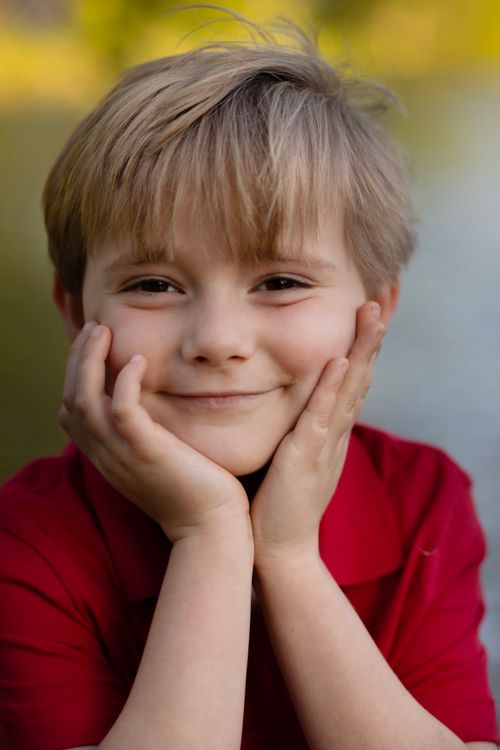 Free A young boy in a red shirt smiles warmly with hands on face outdoors. Stock Photo
