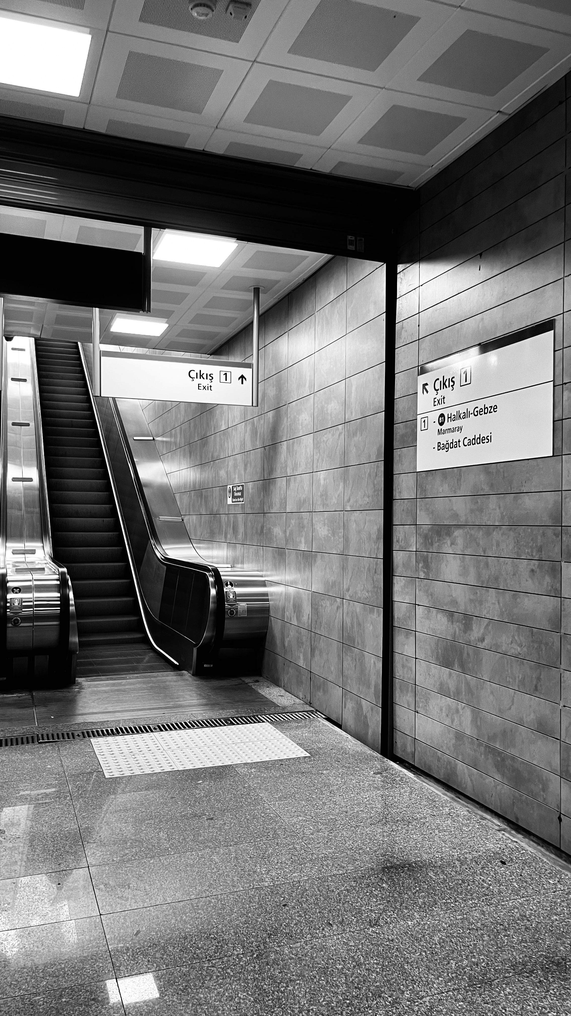 Black and white photo of a subway station with an escalator and directional signs.