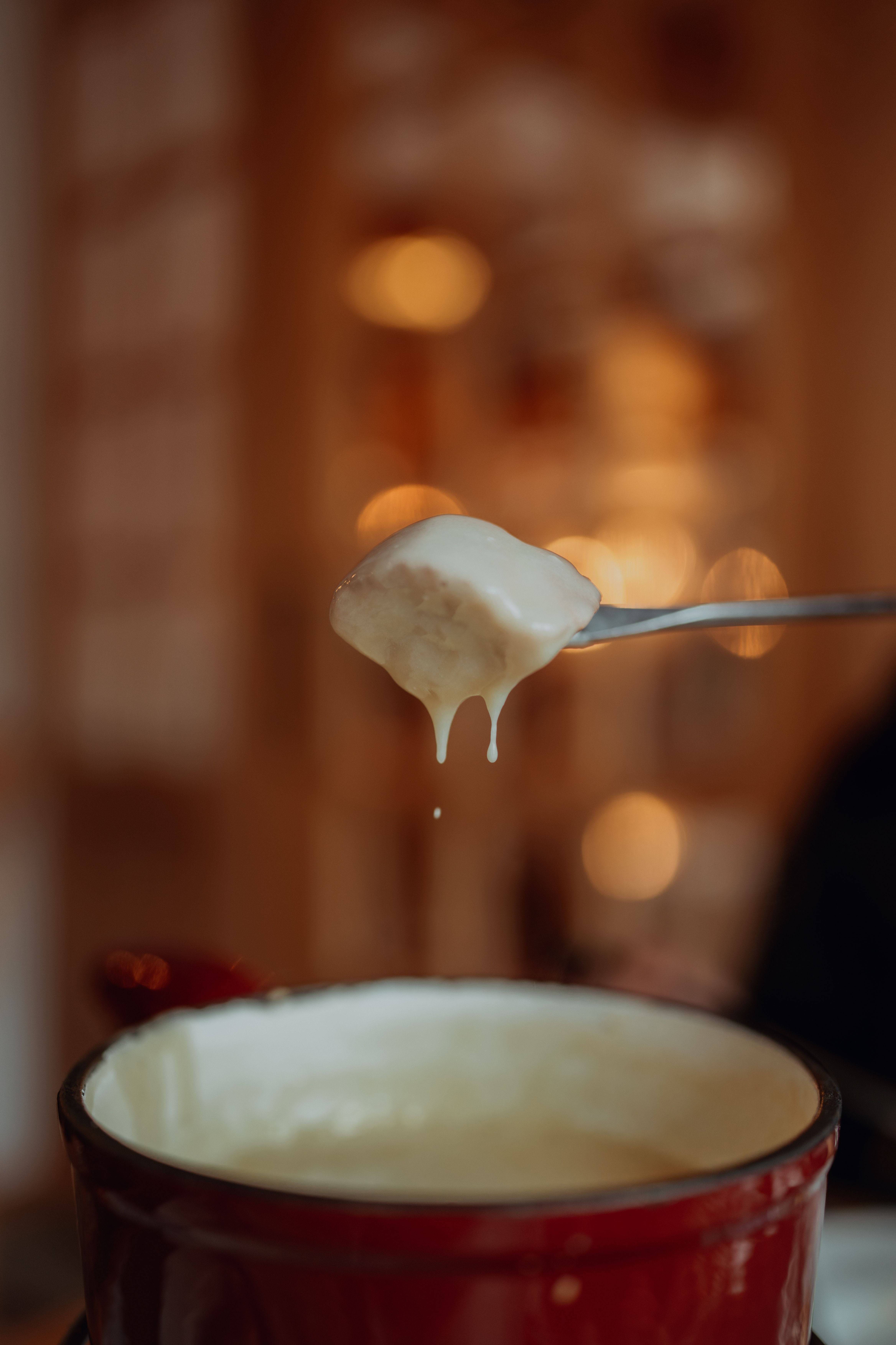 Close-up of cheese fondue with bread on fork, creating a cozy indoor ambiance.
