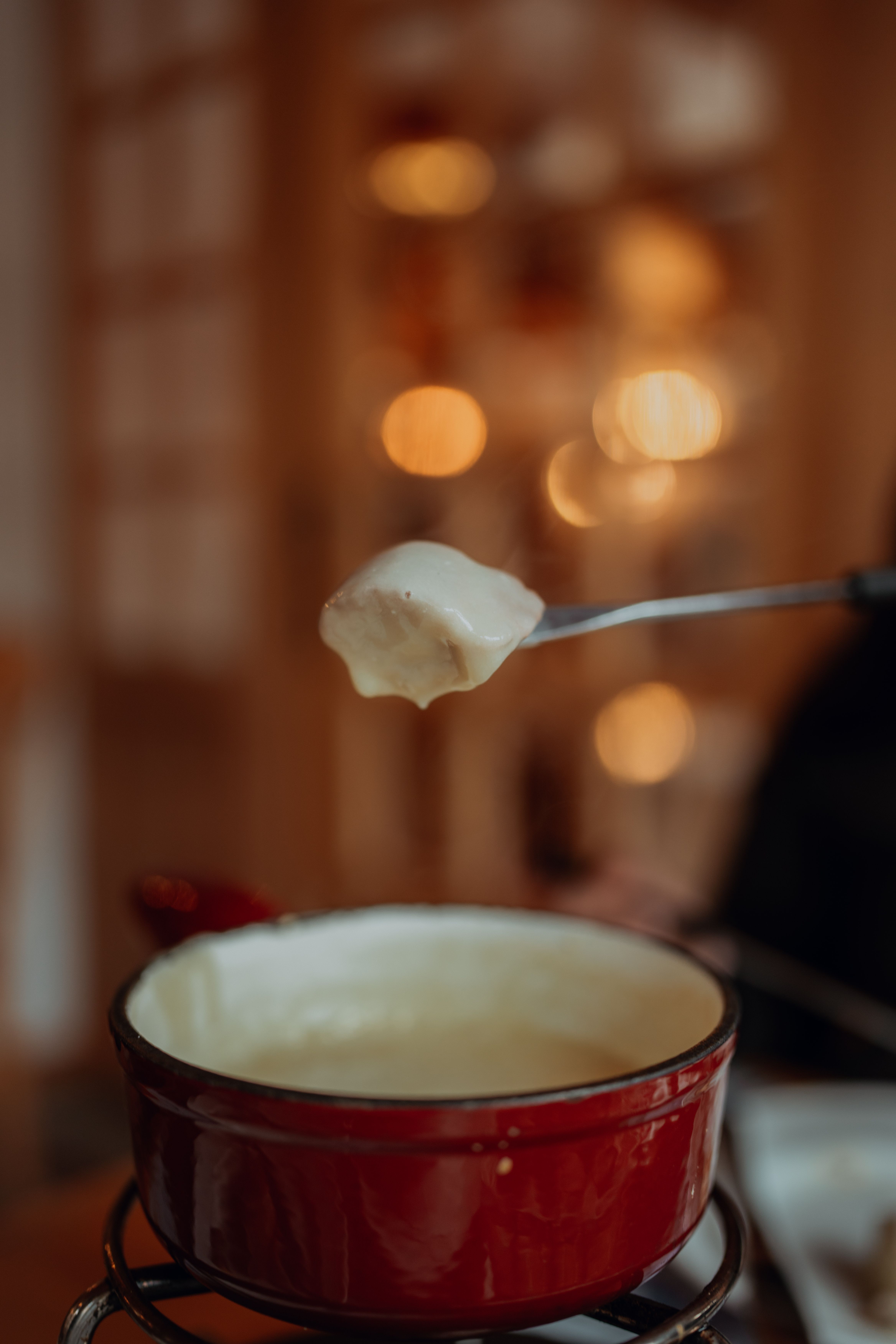 Warm cheese fondue in a red pot with blurred lights creating a cozy atmosphere.