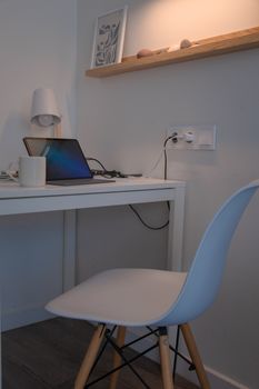 Stylish home office with a minimalist white desk, laptop, and chair in a cozy corner.