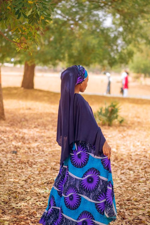 Free Woman in vibrant traditional attire walking in a serene, leafy park. Stock Photo