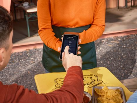 Person using phone for tipping at an outdoor dining table, highlighting contactless payment convenience.