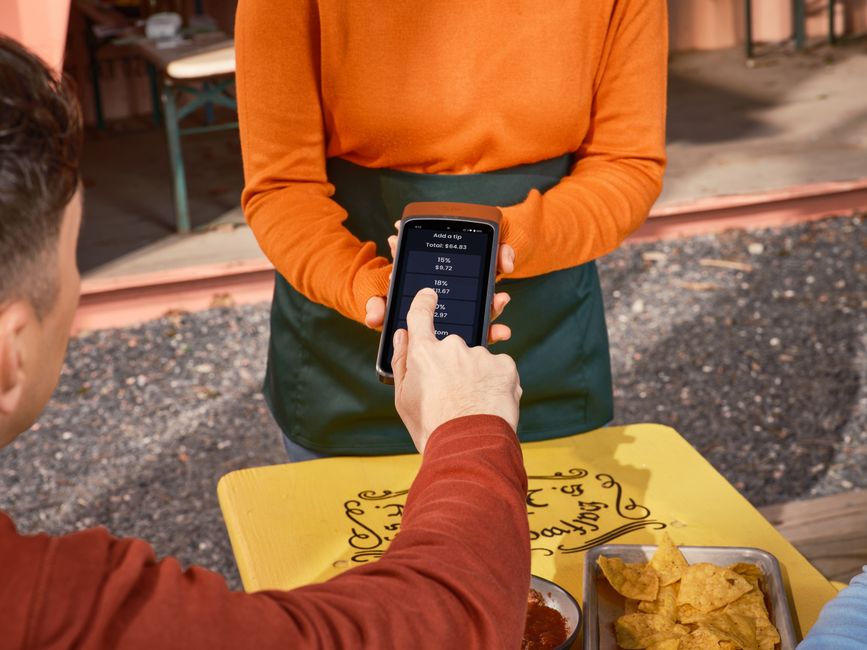 Person using phone for tipping at an outdoor dining table, highlighting contactless payment convenience.