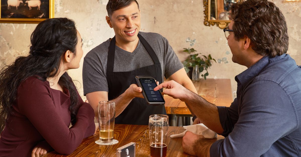 Customers interacting with digital payment system at a cozy, rustic restaurant setting.