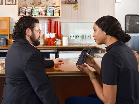 Two adults discussing a handheld point-of-sale system in a restaurant setting.