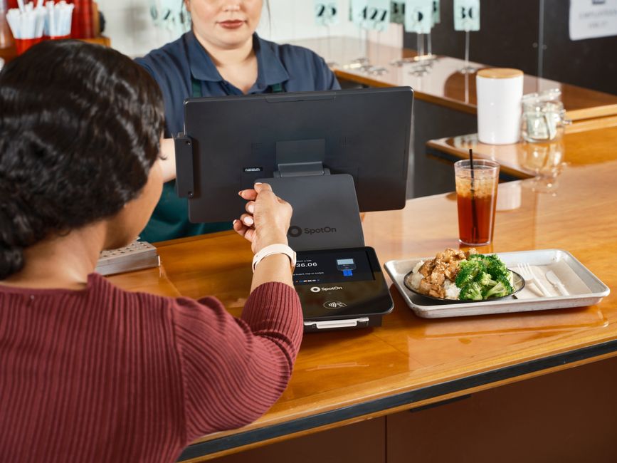 A customer uses smartwatch for contactless payment at a restaurant with SpotOn POS system. A customer uses smartwatch for contactless payment at a restaurant with SpotOn POS system.