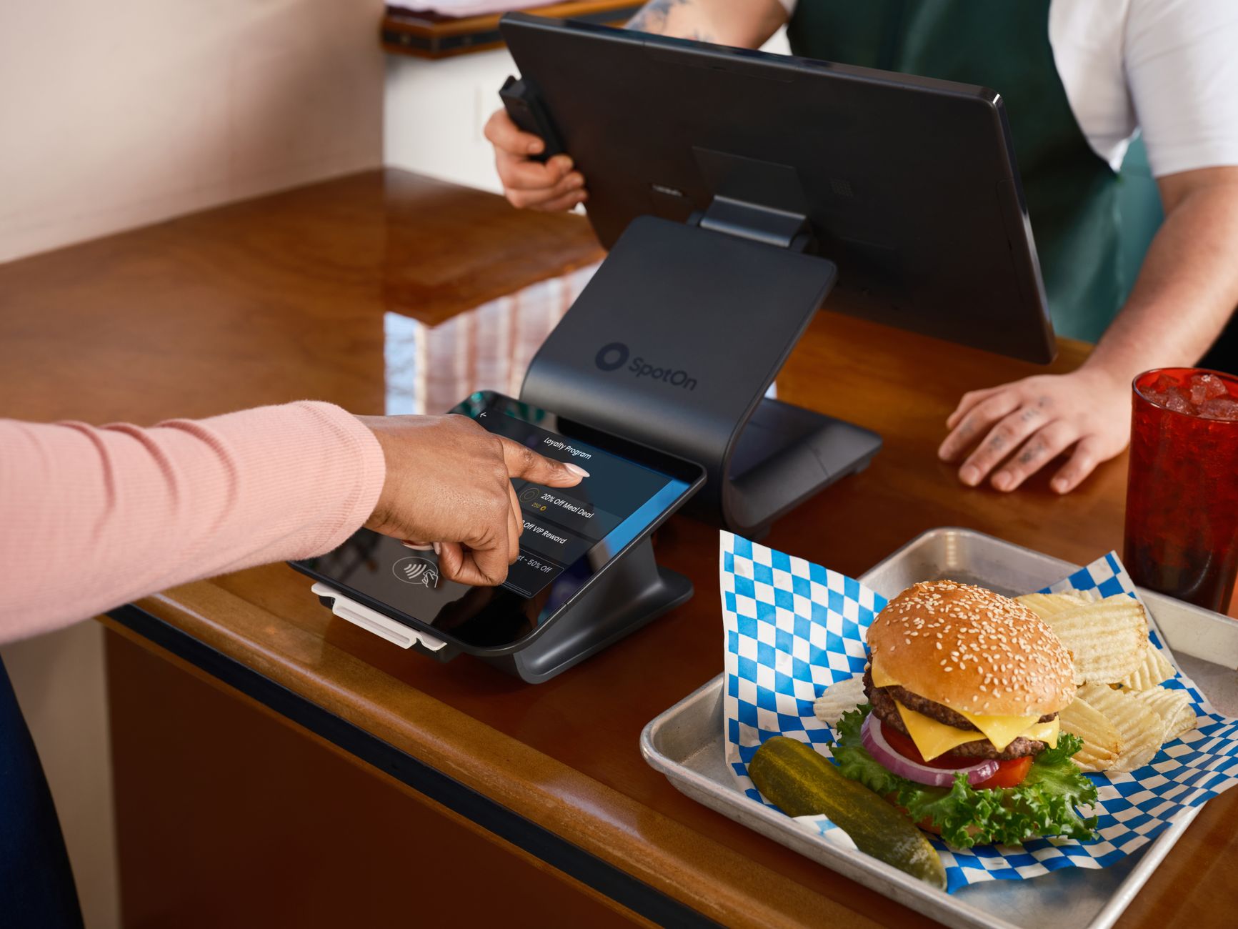Restaurant counter with SpotOn POS system and burger meal, featuring customer interaction.