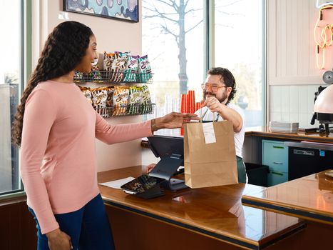 A customer receives a takeout order at a cafe counter, showcasing modern point of sale technology.