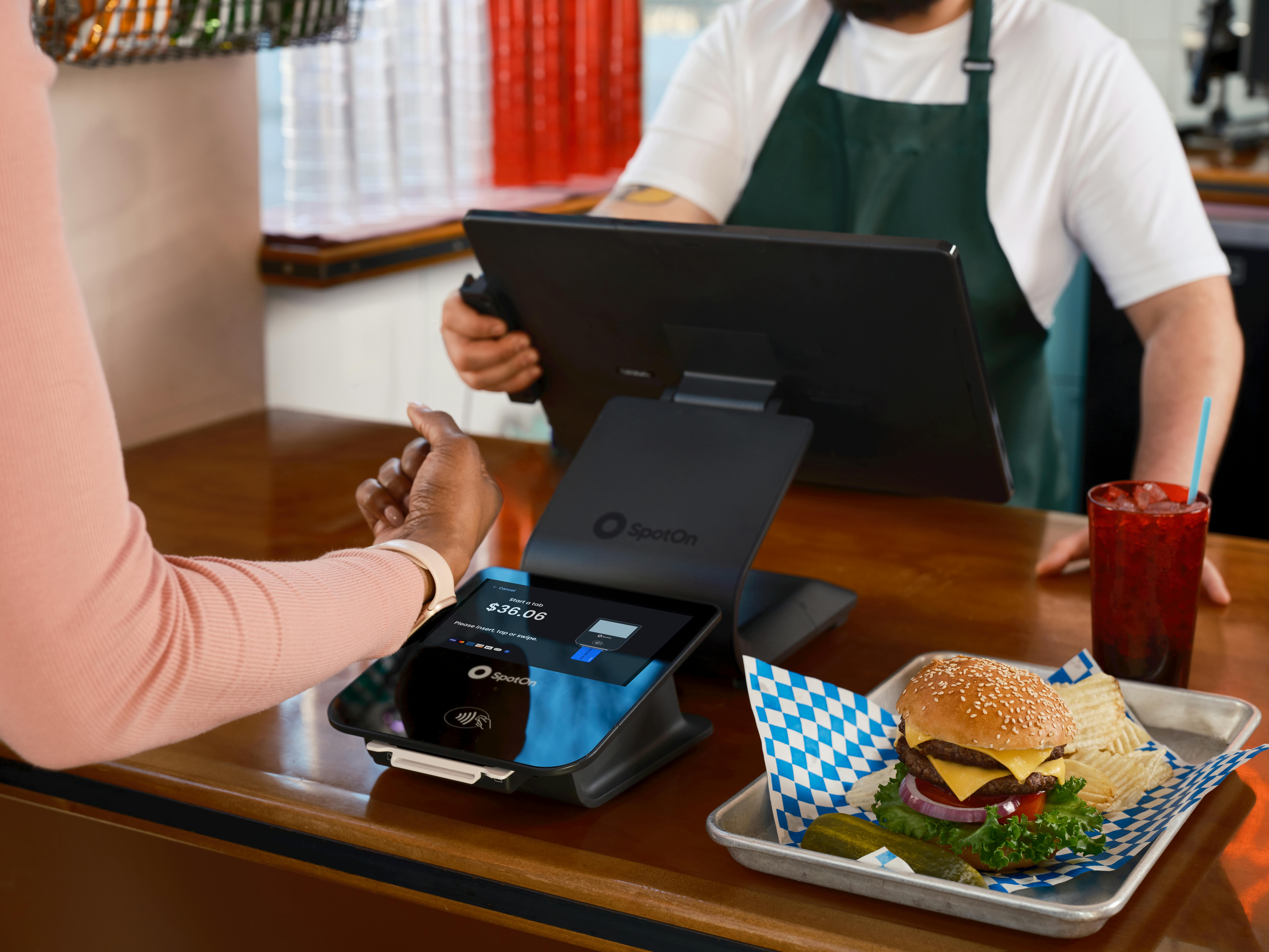 Customer using contactless payment at a restaurant counter with a burger and drink.