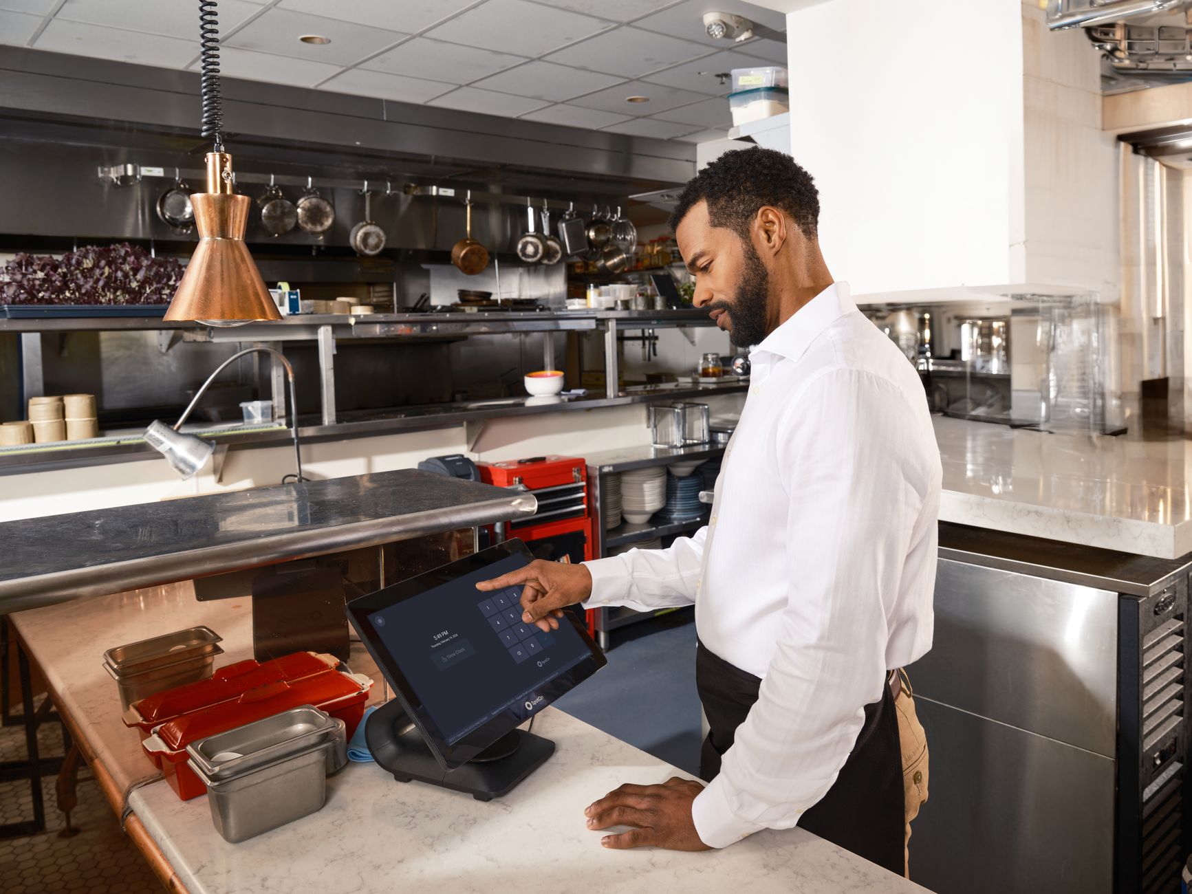 A restaurant worker operates a point of sale system in a commercial kitchen setting.