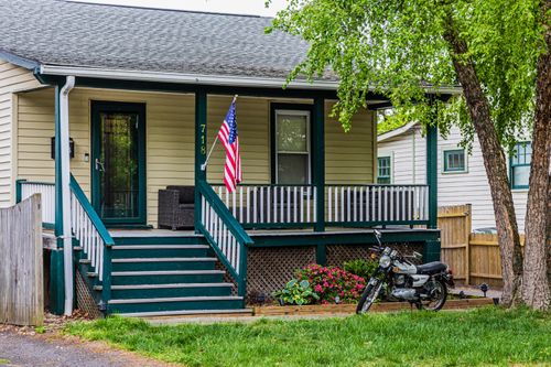 Free A quaint house with a porch, American flag, and motorcycle parked in the green yard. Stock Photo