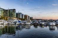 A serene evening view of boats docked at a city marina surrounded by modern buildings.