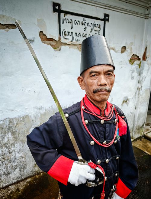 Free Portrait of a traditional guard in historical uniform, holding a sword against an aged wall. Stock Photo