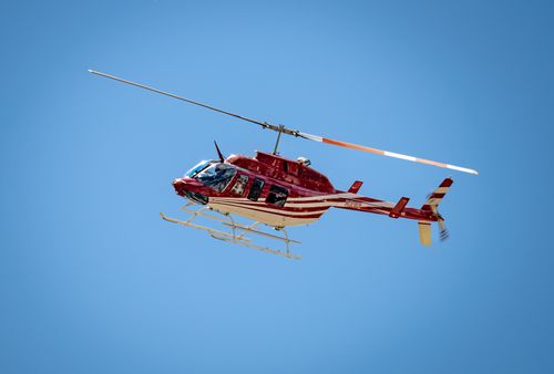 Free A red Bell 206 helicopter soaring against a clear blue sky, showcasing aviation in action. Stock Photo