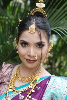Portrait of a woman wearing traditional Indian attire and jewelry, set outdoors.