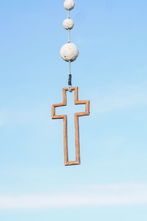 Free A minimalistic wooden cross pendant suspended in front of a bright blue sky. Stock Photo
