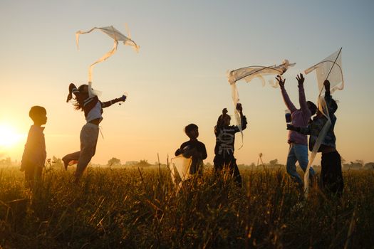 Joyful children fly kites at sunset in a Cambodian field, capturing carefree childhood moments.