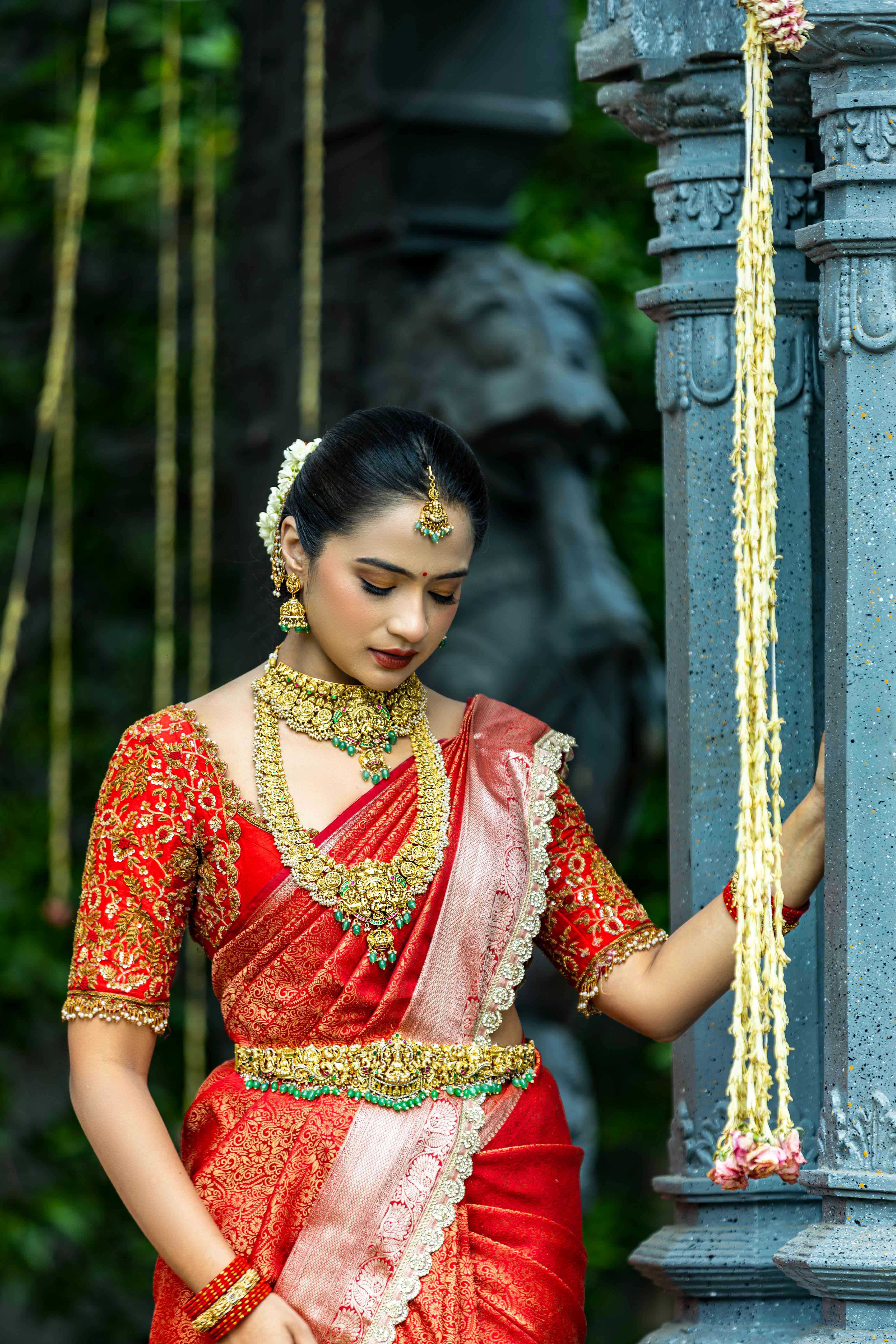 Elegant Indian bride in red sari with intricate jewelry, captured outdoors.