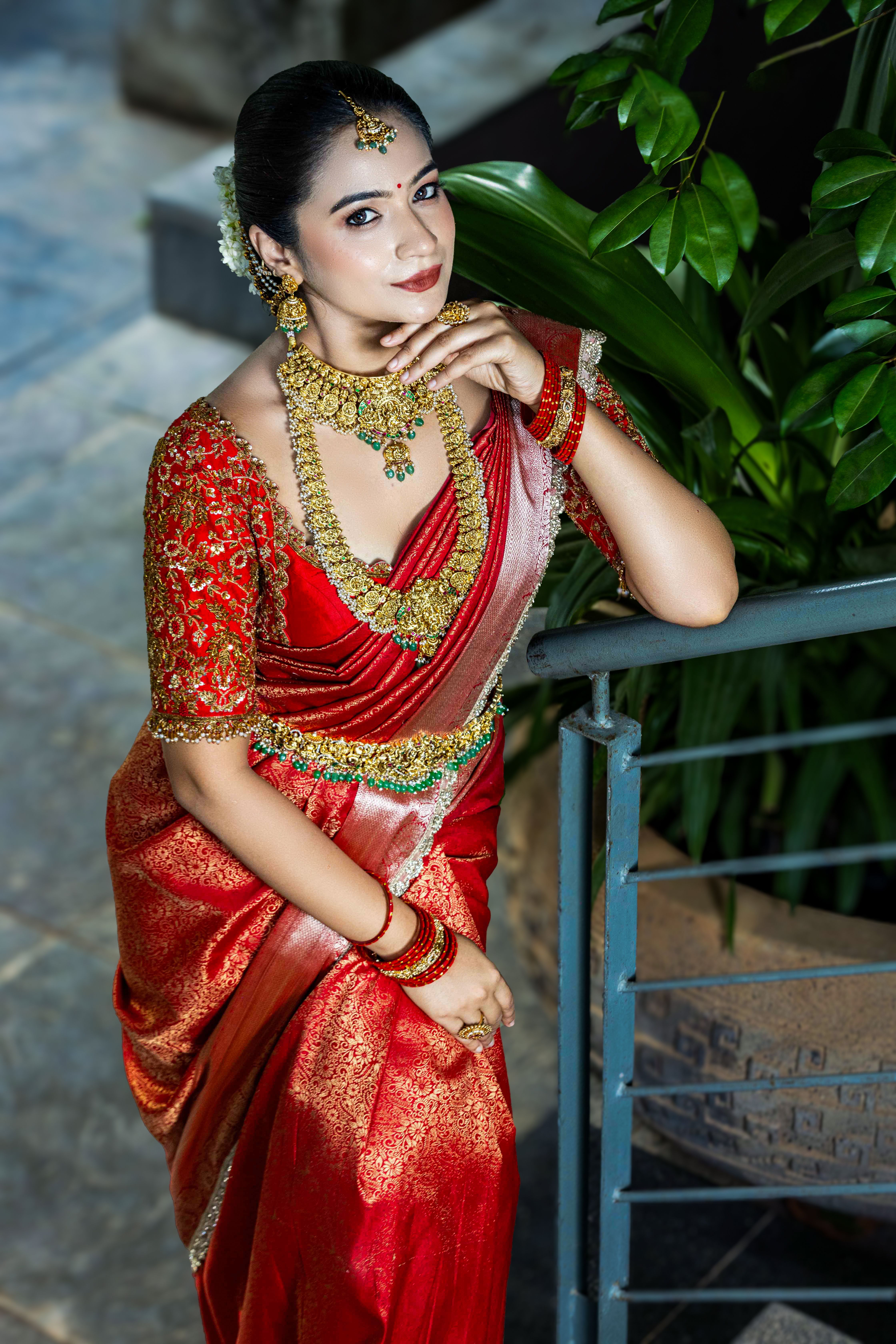 Graceful Indian bride in a luxurious red saree with gold jewelry, indoors.
