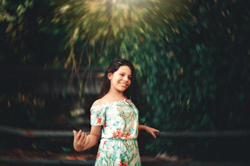 Selective Focus Photo of Smiling Girl in Floral Dress Standing by Railing