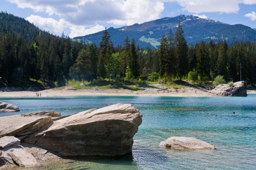 Breathtaking view of Caumasee in Flims, Switzerland, with clear water, forest backdrop, and distant mountains.