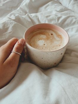 Warm coffee cup held in bed, embracing a cozy morning vibe.