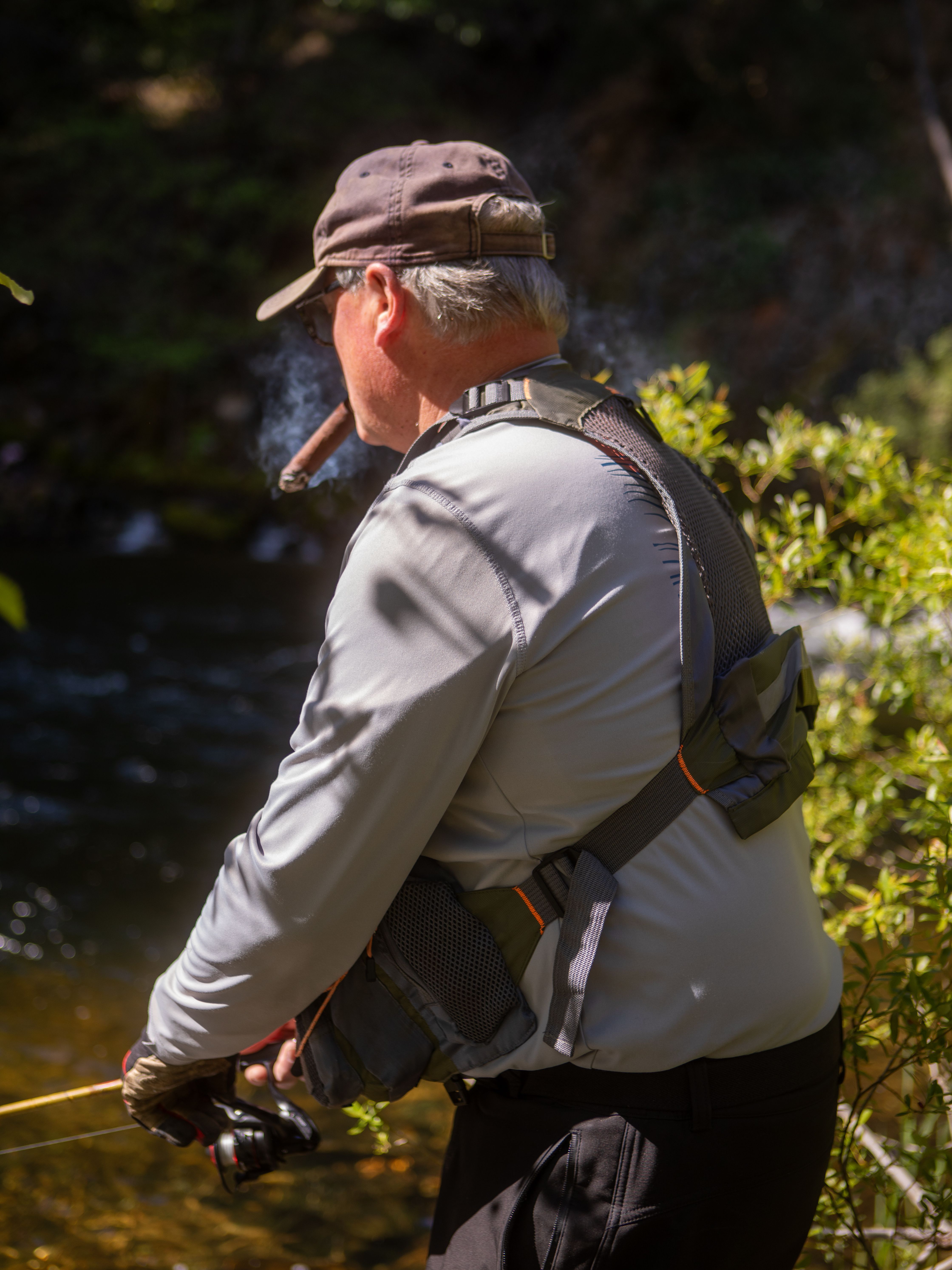 Adult man enjoys fly fishing by a river surrounded by lush greenery, California.