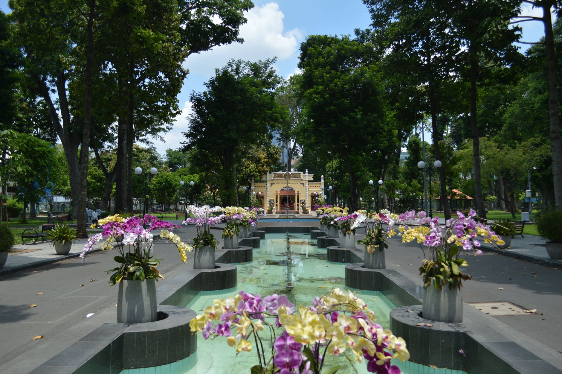 A tranquil garden scene featuring colorful orchids and fountains with lush greenery highlighting a sunny day.