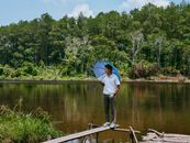 A man holds an umbrella while standing on a rustic dock by a tranquil forest lake.