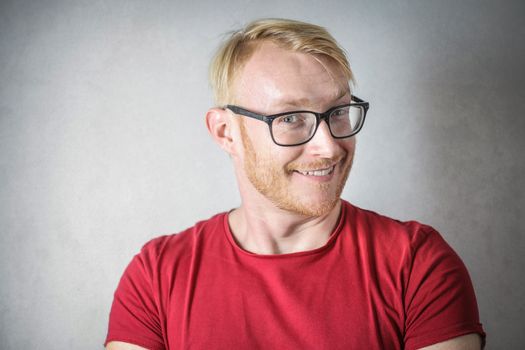 Portrait of a young blonde man in red shirt smiling with eyeglasses.