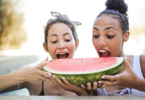 Free Two women having fun eating watermelon outdoors by the pool. Stock Photo