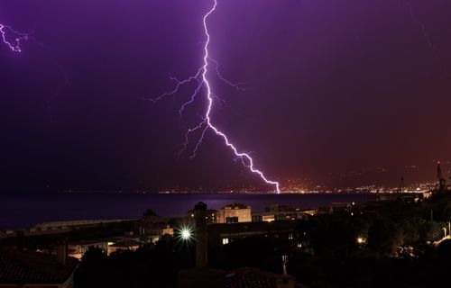 Free Thunderstorm and lighting bolt striking over sea in coastal city against dark purple night sky Stock Photo