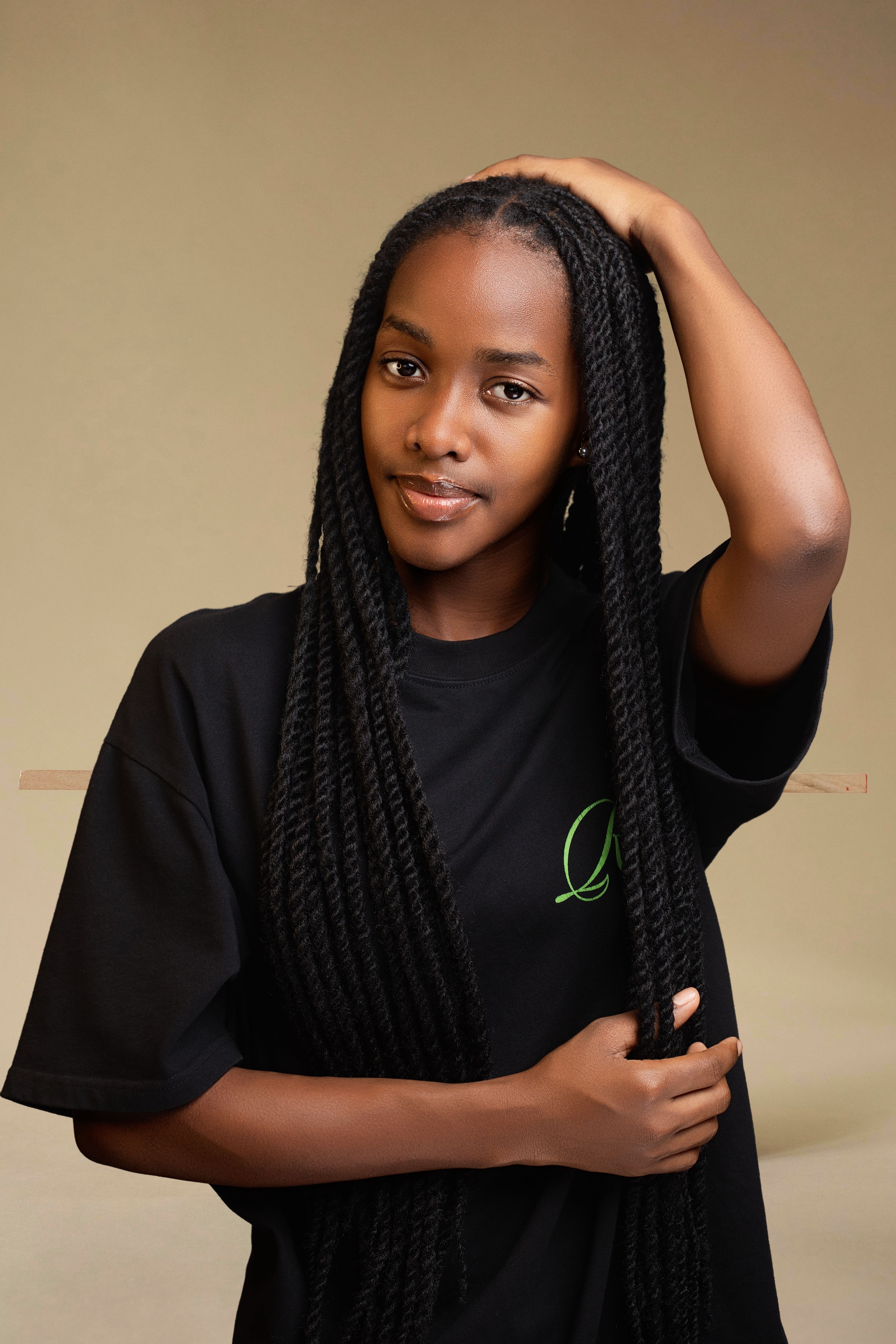 Close-up portrait of a young woman wearing a black shirt with long braided hair posing indoors.