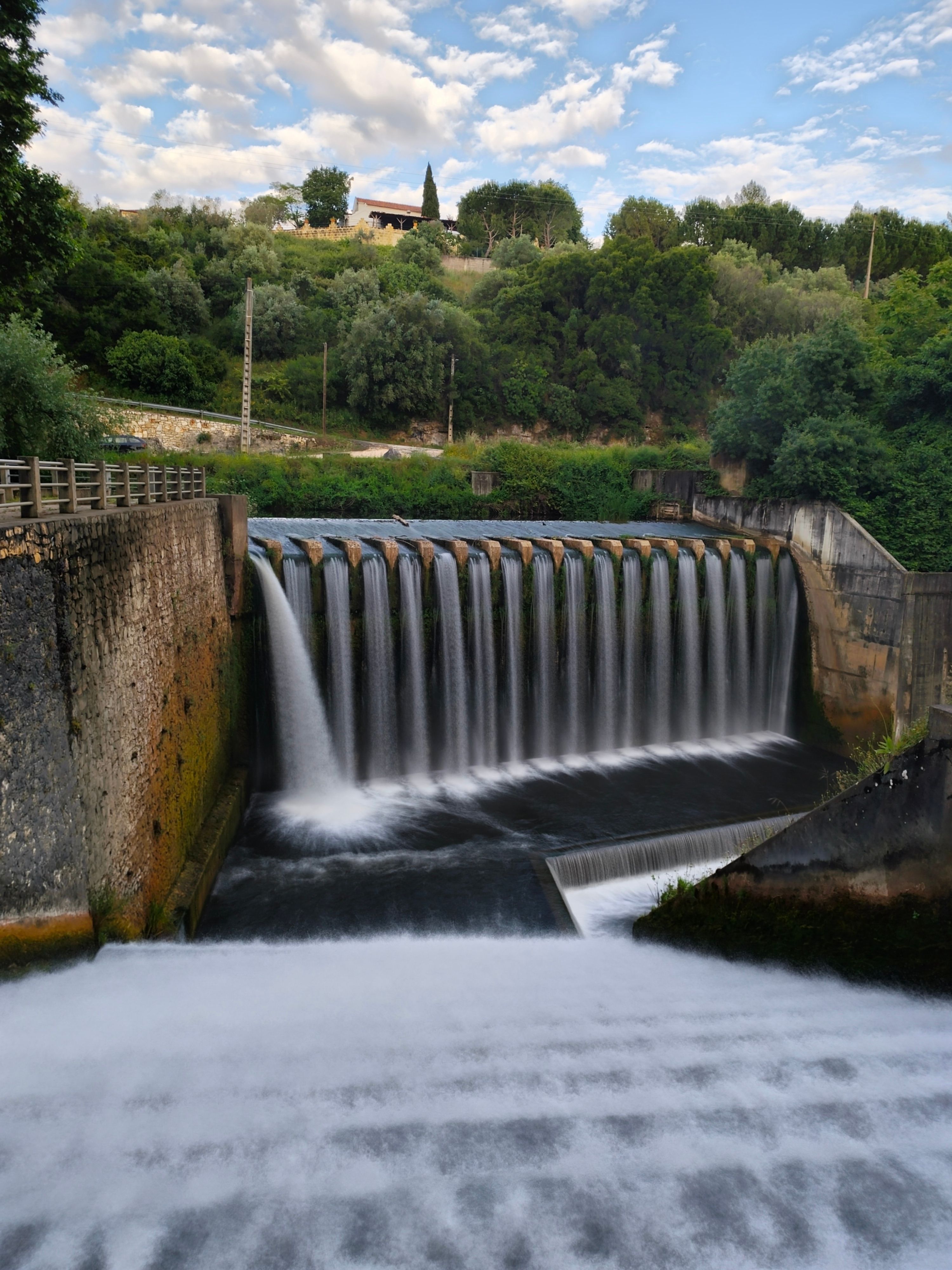 A picturesque waterfall dam amidst lush trees and serene surroundings, perfect for nature themes.